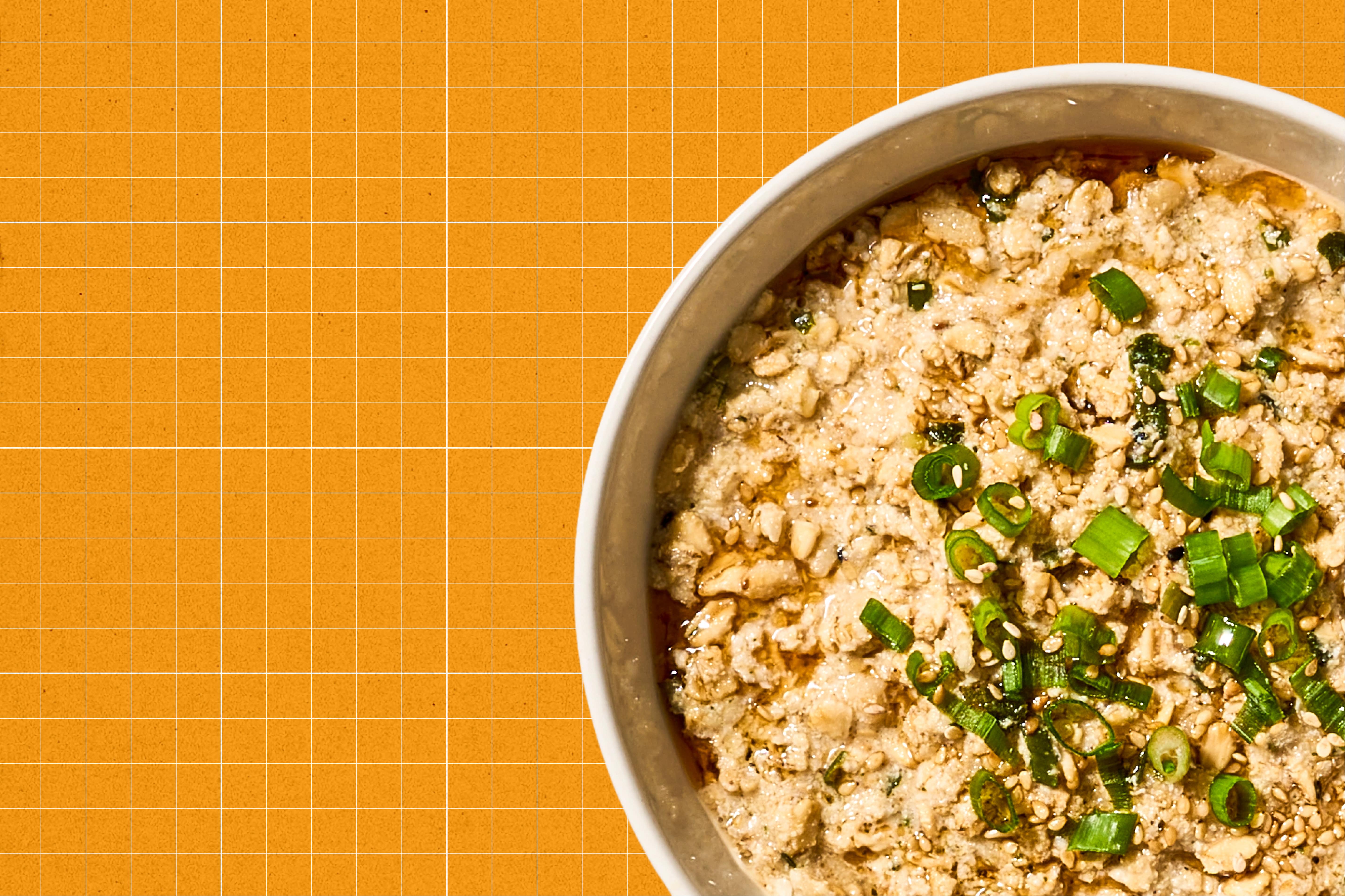 Bowl of Gamsa Korean oatmeal with green onions on an orange grid background